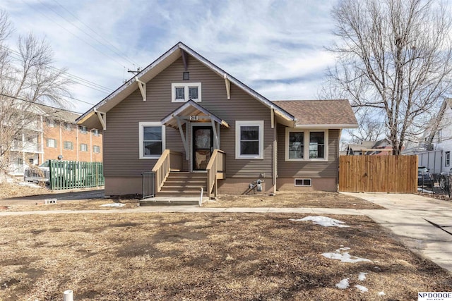 bungalow-style home with roof with shingles and fence