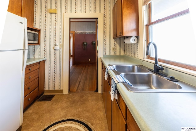 kitchen featuring wallpapered walls, brown cabinetry, light countertops, and freestanding refrigerator