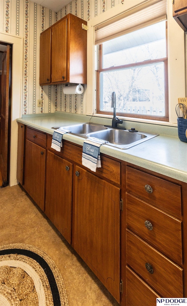 kitchen with brown cabinetry, light countertops, a sink, and wallpapered walls