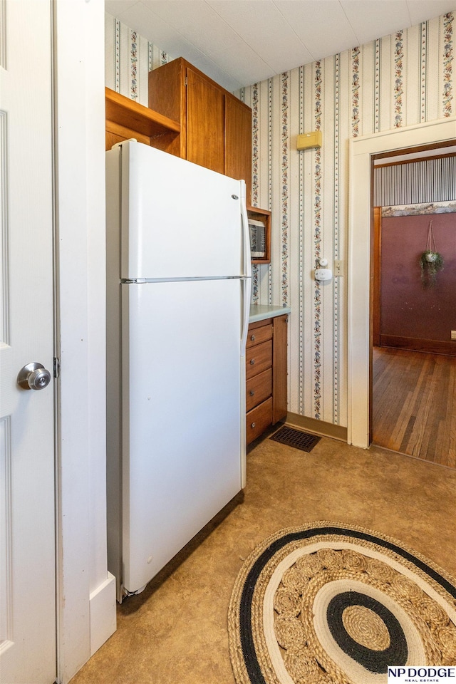 kitchen with light countertops, brown cabinets, freestanding refrigerator, and wallpapered walls