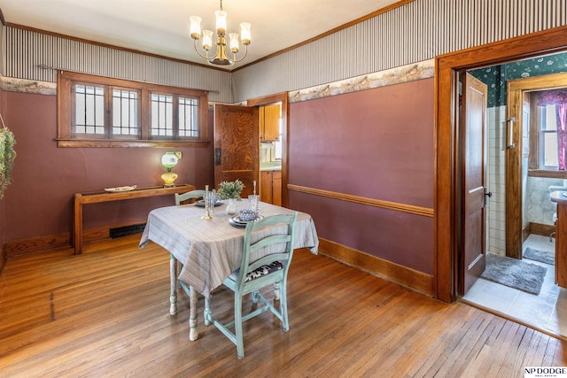 dining area with baseboards, wallpapered walls, hardwood / wood-style floors, and an inviting chandelier