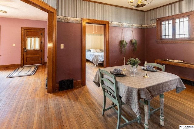 dining room featuring wallpapered walls, hardwood / wood-style floors, visible vents, and baseboards