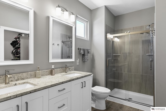 bathroom with double vanity, a stall shower, a sink, and wood finished floors