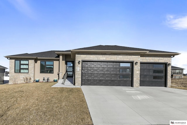 prairie-style home with driveway, stone siding, roof with shingles, an attached garage, and a front yard