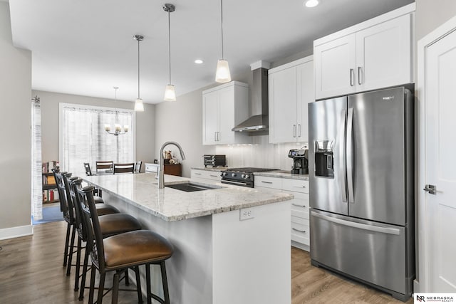 kitchen with white cabinets, a kitchen island with sink, a sink, wall chimney range hood, and stainless steel fridge with ice dispenser