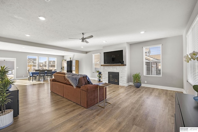 living room with a textured ceiling, a stone fireplace, wood finished floors, and baseboards