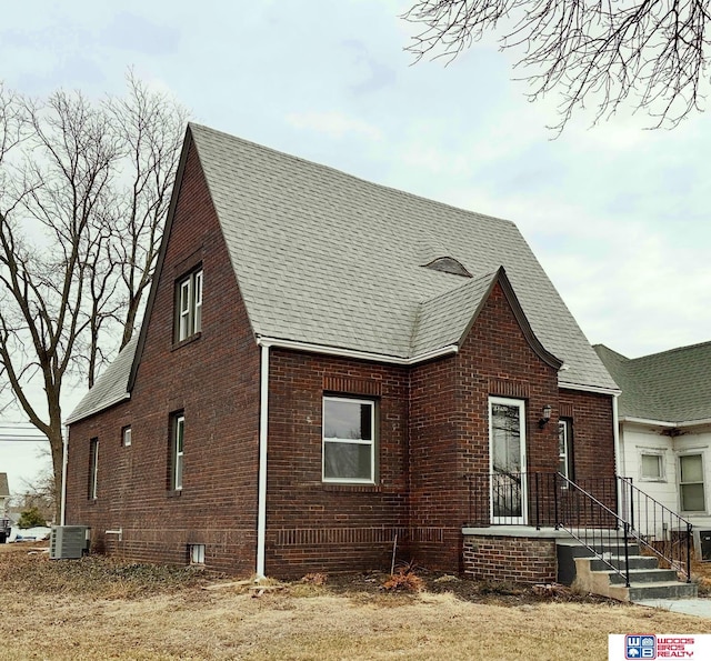 view of front of home with a shingled roof, central AC, and brick siding