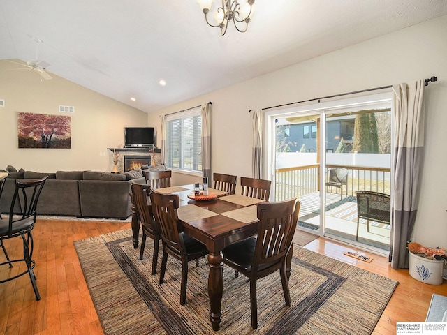 dining room featuring lofted ceiling, light wood-style flooring, a glass covered fireplace, and visible vents