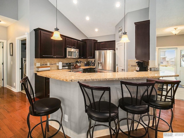 kitchen with a peninsula, decorative backsplash, stainless steel appliances, and dark wood-style flooring