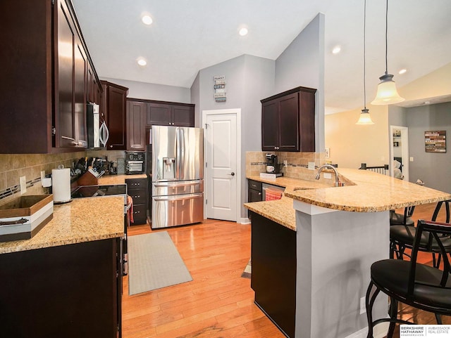 kitchen with appliances with stainless steel finishes, pendant lighting, a breakfast bar area, and light stone countertops