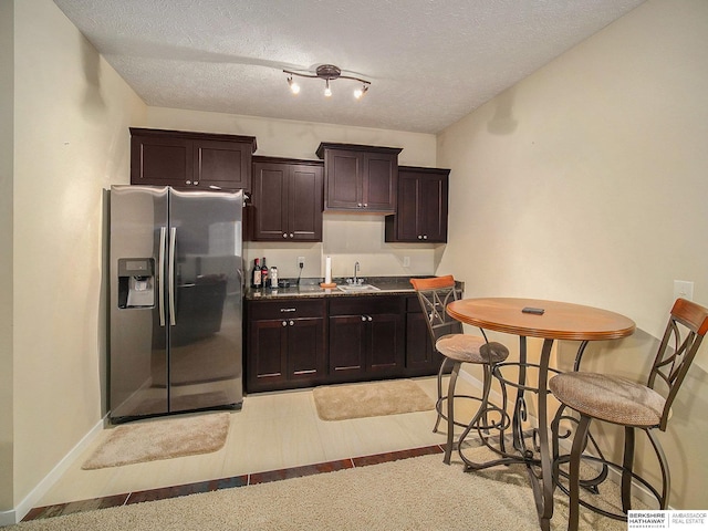 kitchen featuring a textured ceiling, stainless steel refrigerator with ice dispenser, a sink, and dark brown cabinetry