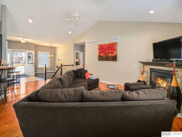 living area featuring lofted ceiling, light wood finished floors, visible vents, and a stone fireplace