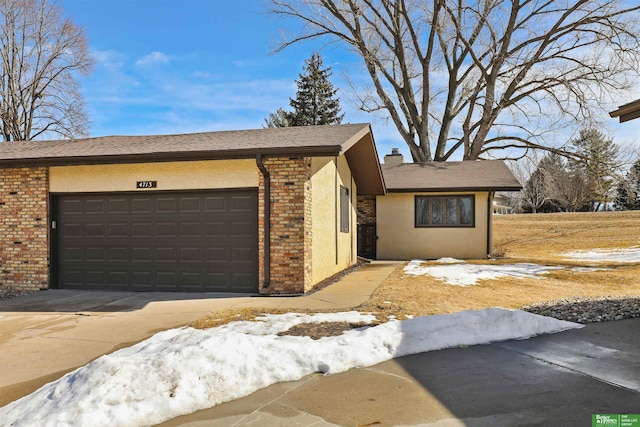 view of front of property with brick siding, a chimney, stucco siding, concrete driveway, and an attached garage