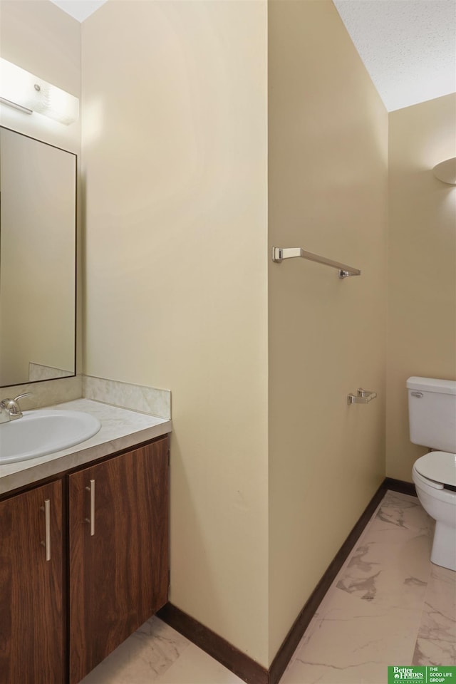 bathroom with marble finish floor, toilet, vanity, and baseboards