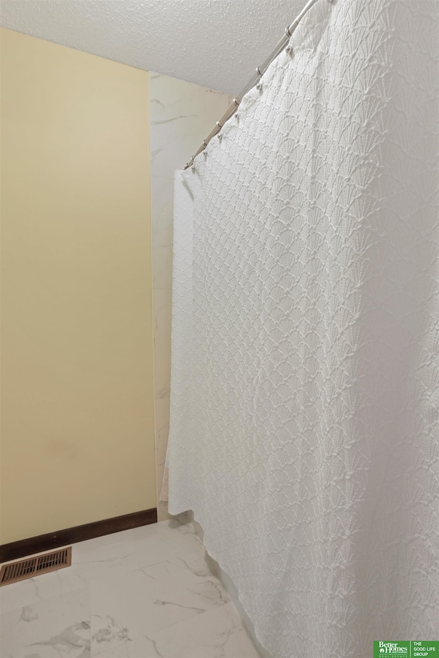 bathroom with marble finish floor, visible vents, a textured ceiling, and baseboards