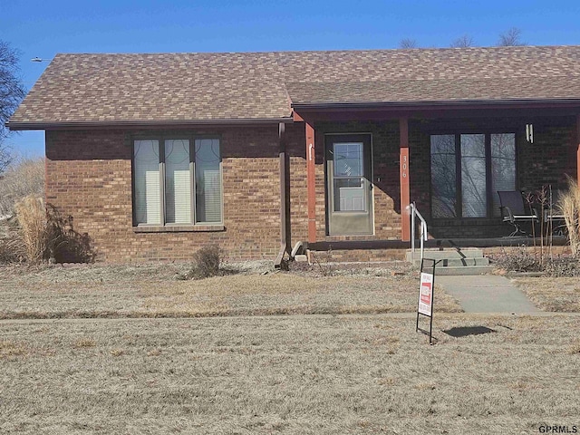 ranch-style house with entry steps, a shingled roof, a front yard, and brick siding