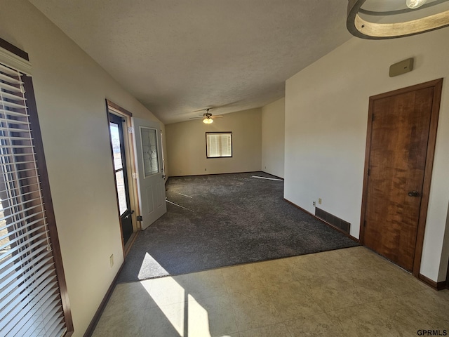 empty room with dark carpet, vaulted ceiling, a textured ceiling, ceiling fan, and baseboards