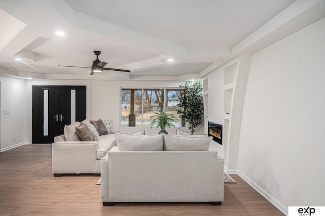 living room featuring light wood finished floors, ceiling fan, baseboards, and a glass covered fireplace