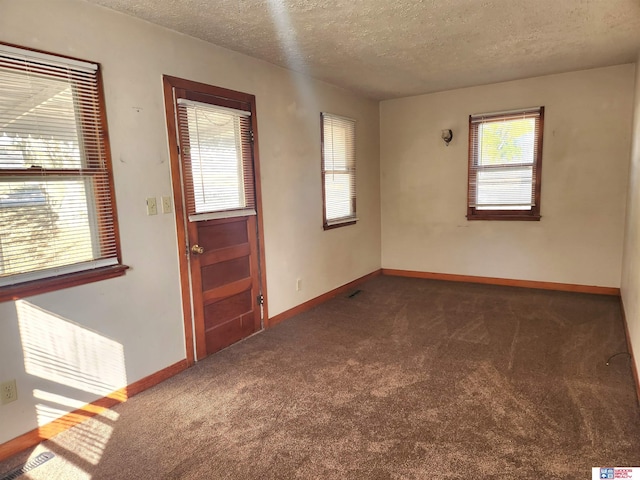 spare room with baseboards, dark colored carpet, and a textured ceiling