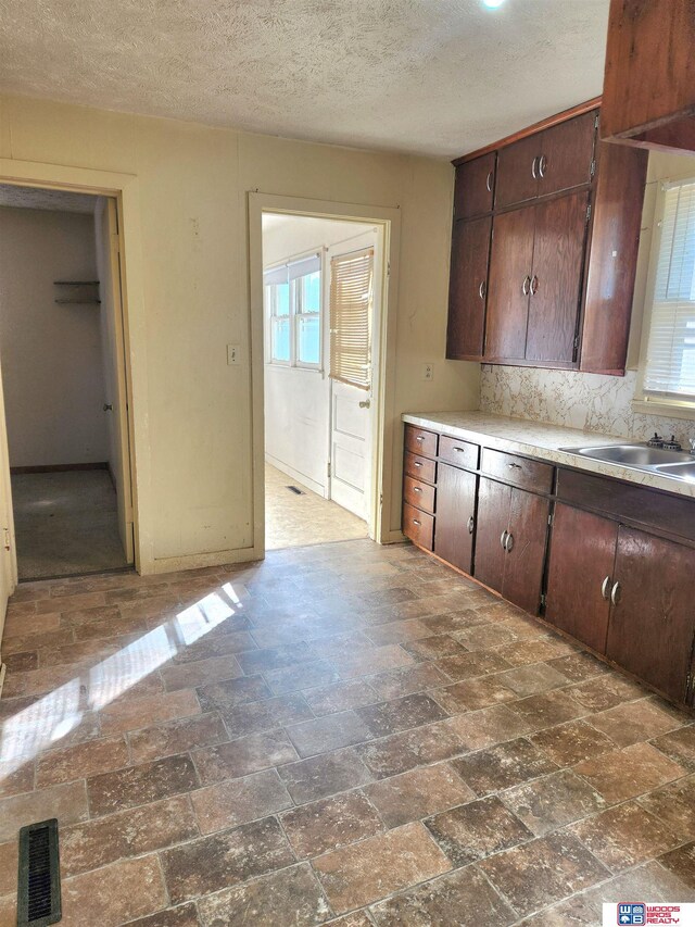 kitchen featuring visible vents, light countertops, a textured ceiling, dark brown cabinets, and a sink