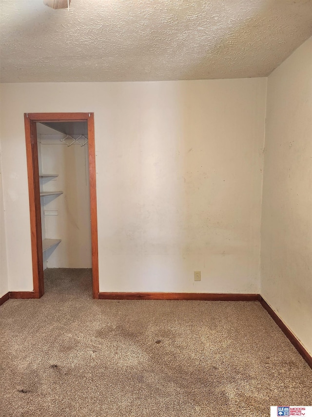 empty room with carpet, baseboards, and a textured ceiling