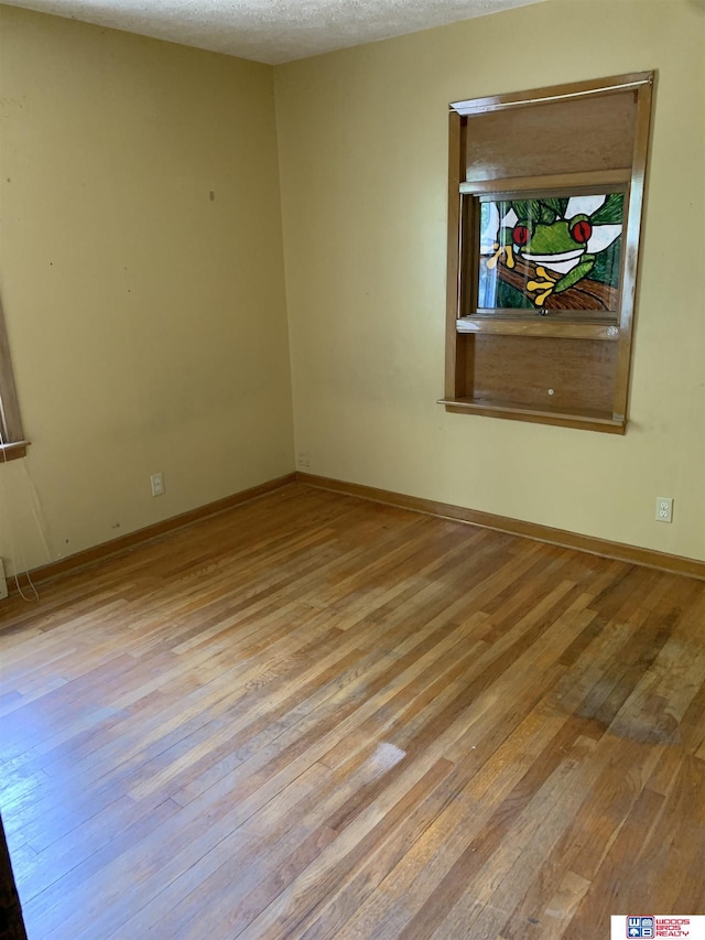 spare room featuring light wood-type flooring, a textured ceiling, and baseboards