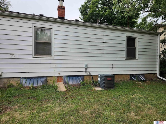 view of side of home with a lawn, a chimney, and central air condition unit