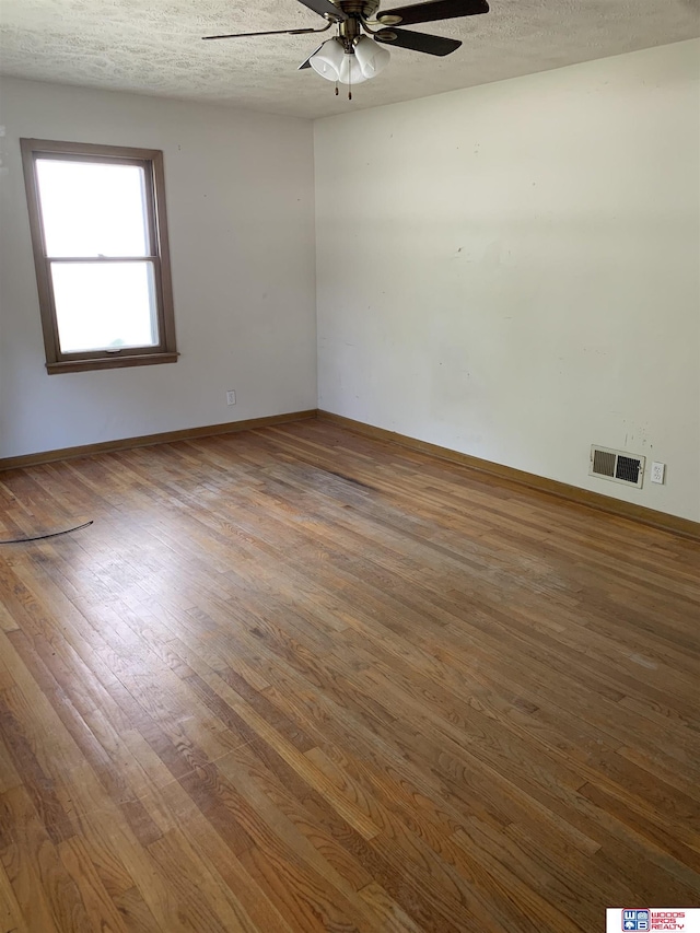 unfurnished room with baseboards, visible vents, a ceiling fan, wood finished floors, and a textured ceiling