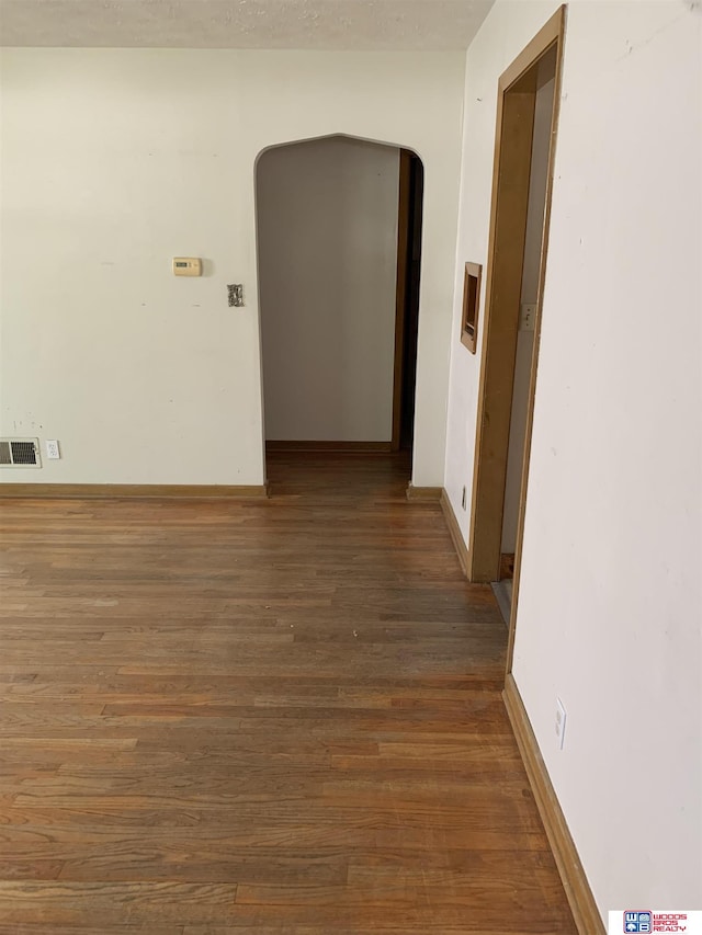 hall with arched walkways, dark wood finished floors, visible vents, and baseboards