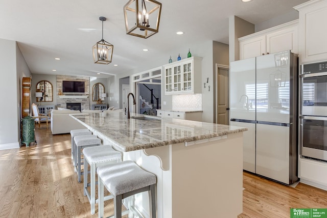 kitchen featuring a fireplace, freestanding refrigerator, a sink, double oven, and light wood-type flooring