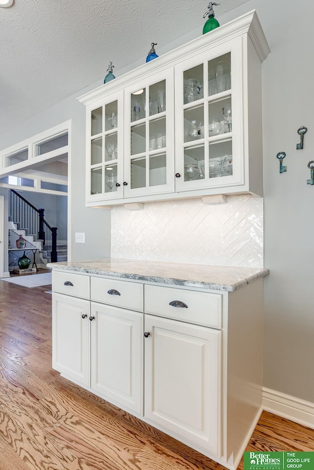 bar featuring decorative backsplash, light wood-style flooring, a textured ceiling, and baseboards