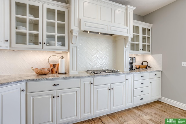 kitchen with baseboards, stainless steel gas cooktop, light wood-style flooring, white cabinets, and glass insert cabinets