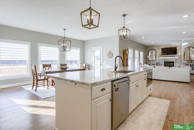 kitchen with dishwasher, a stone fireplace, light wood-style floors, hanging light fixtures, and a sink