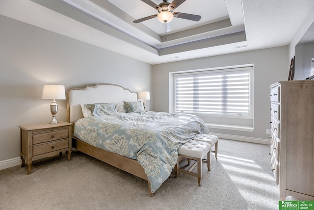 bedroom featuring light colored carpet, baseboards, a tray ceiling, and ceiling fan