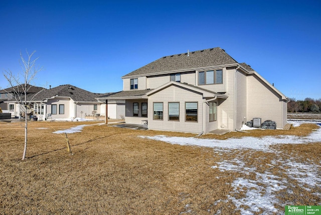 snow covered rear of property featuring a patio, central air condition unit, and a shingled roof