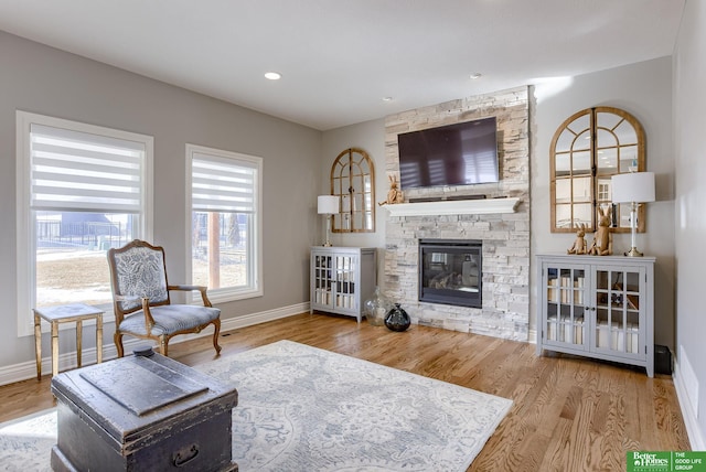 living area featuring a stone fireplace, recessed lighting, baseboards, and wood finished floors