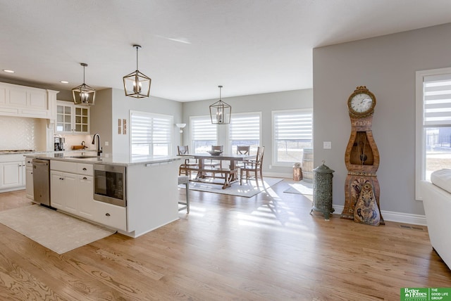 kitchen with a center island with sink, built in microwave, light wood finished floors, and a sink