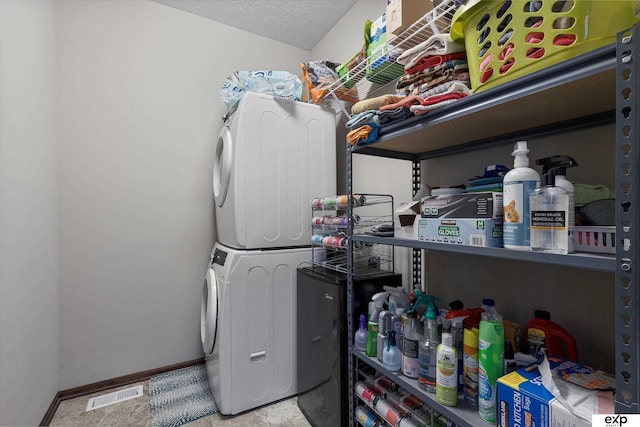 laundry area with laundry area, stacked washer and dryer, baseboards, visible vents, and a textured ceiling