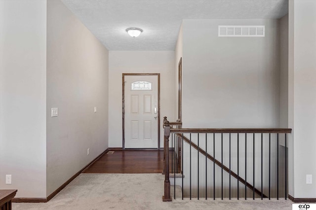 doorway to outside with baseboards, a textured ceiling, visible vents, and carpet flooring