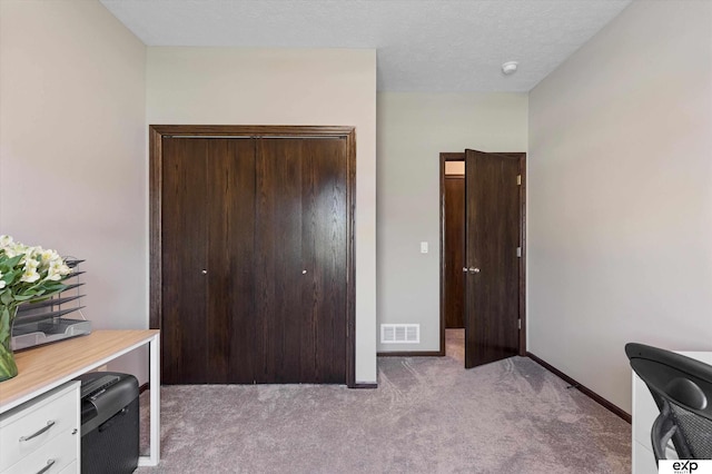 office space with baseboards, a textured ceiling, visible vents, and light colored carpet