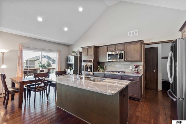 kitchen featuring a sink, visible vents, dark brown cabinets, appliances with stainless steel finishes, and an island with sink