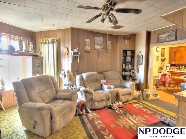 living room with ceiling fan, wooden walls, and visible vents