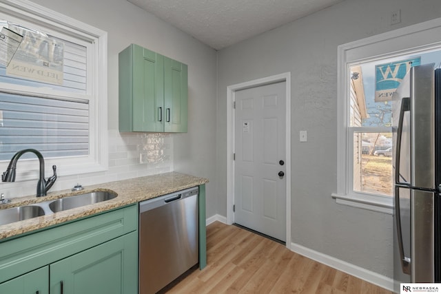 kitchen with decorative backsplash, appliances with stainless steel finishes, light wood-style floors, a sink, and green cabinetry