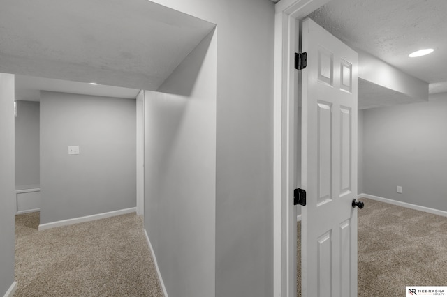 hall featuring light carpet, a textured ceiling, and baseboards