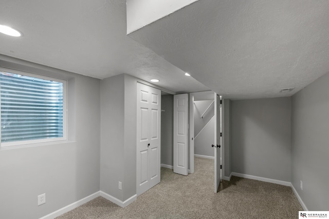 basement featuring a textured ceiling, light carpet, and baseboards