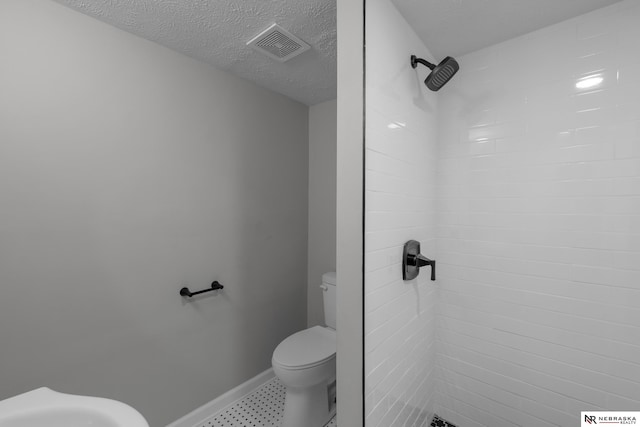 full bathroom featuring visible vents, toilet, a textured ceiling, tiled shower, and baseboards