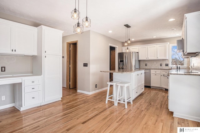 kitchen with stainless steel appliances, a kitchen island, white cabinets, backsplash, and built in desk