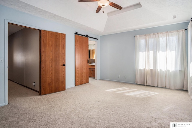 unfurnished bedroom featuring a textured ceiling, a barn door, light colored carpet, baseboards, and a tray ceiling