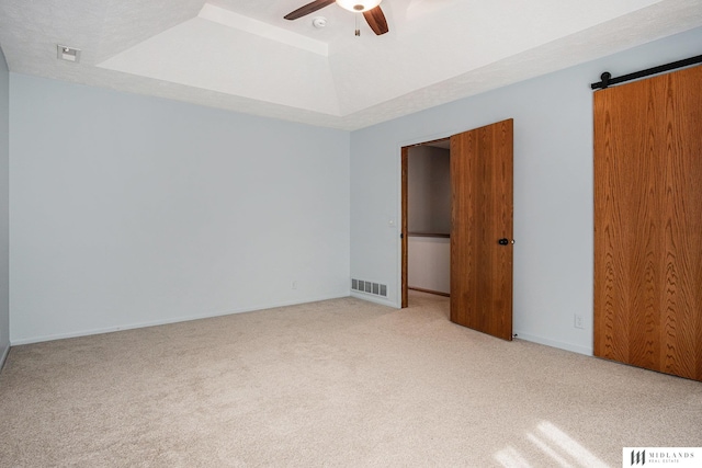 unfurnished bedroom with a raised ceiling, light colored carpet, visible vents, and a barn door