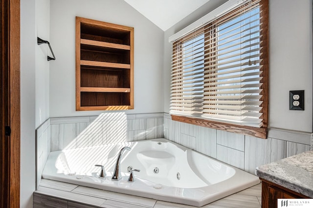 full bath with built in shelves, a wainscoted wall, vaulted ceiling, vanity, and a whirlpool tub